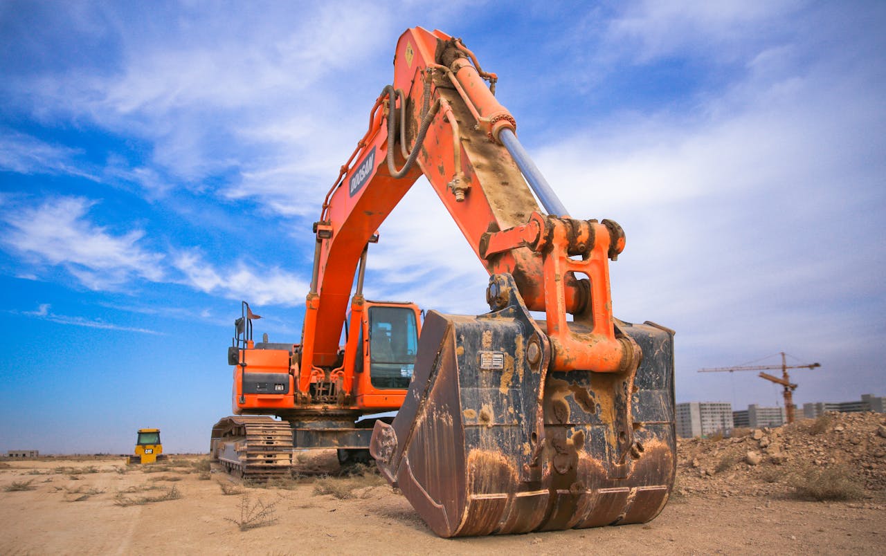 services-02 A large orange excavator working on a construction site under a blue sky.