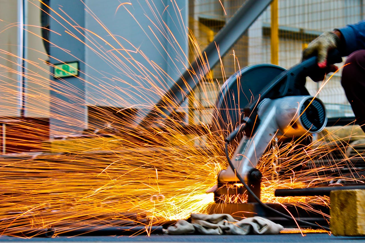 services-01 A worker operates a grinder cutting metal, creating a vibrant display of sparks in an industrial setting.